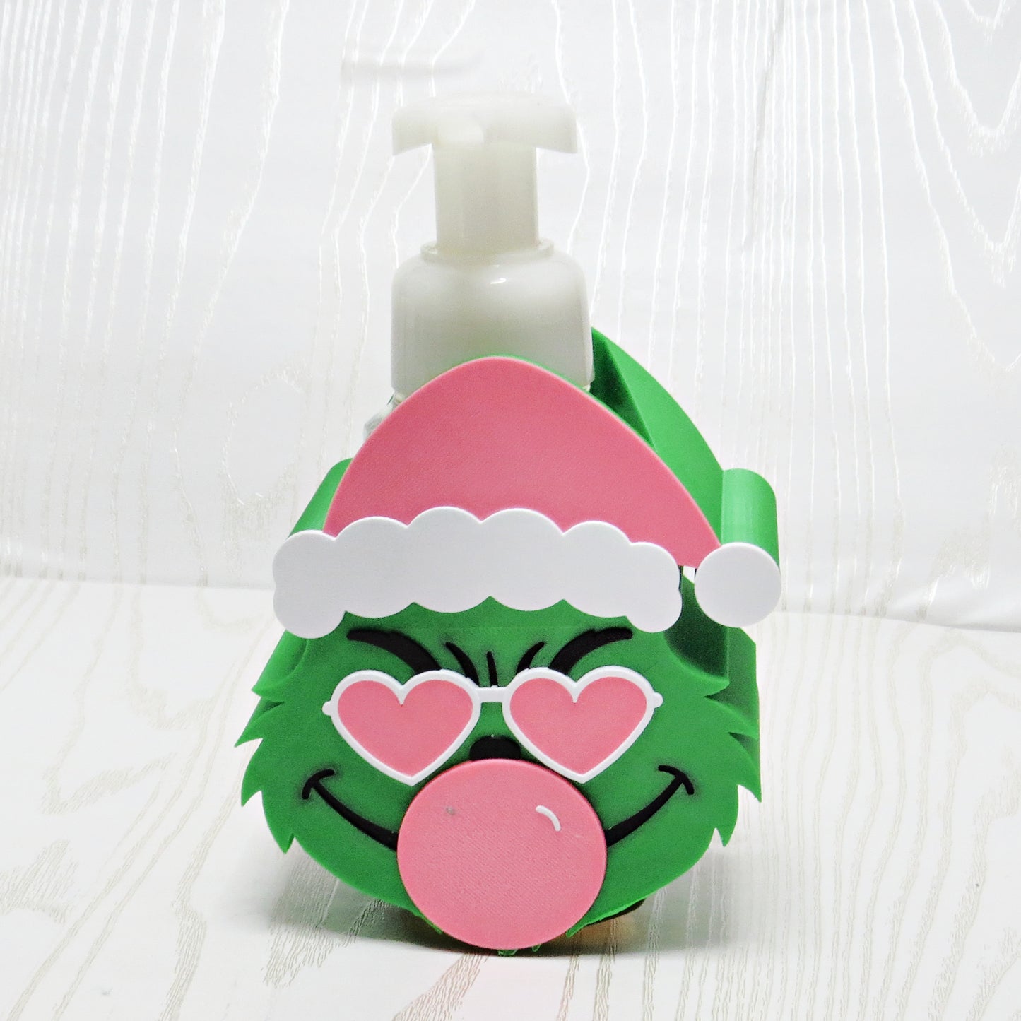 green christmas bubble character foaming soap holder with santa hat and heart sunglasses holding foaming hand soap bottle on white background