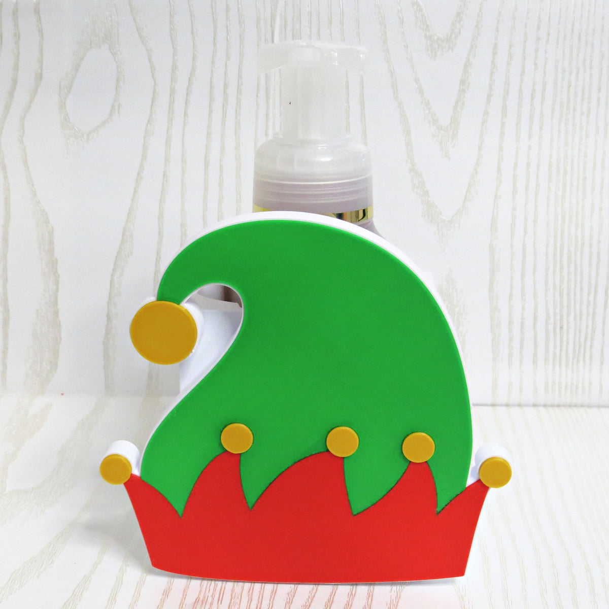 Green and red elf hat shaped foaming soap bottle holder with gold jingle bells for Christmas decor