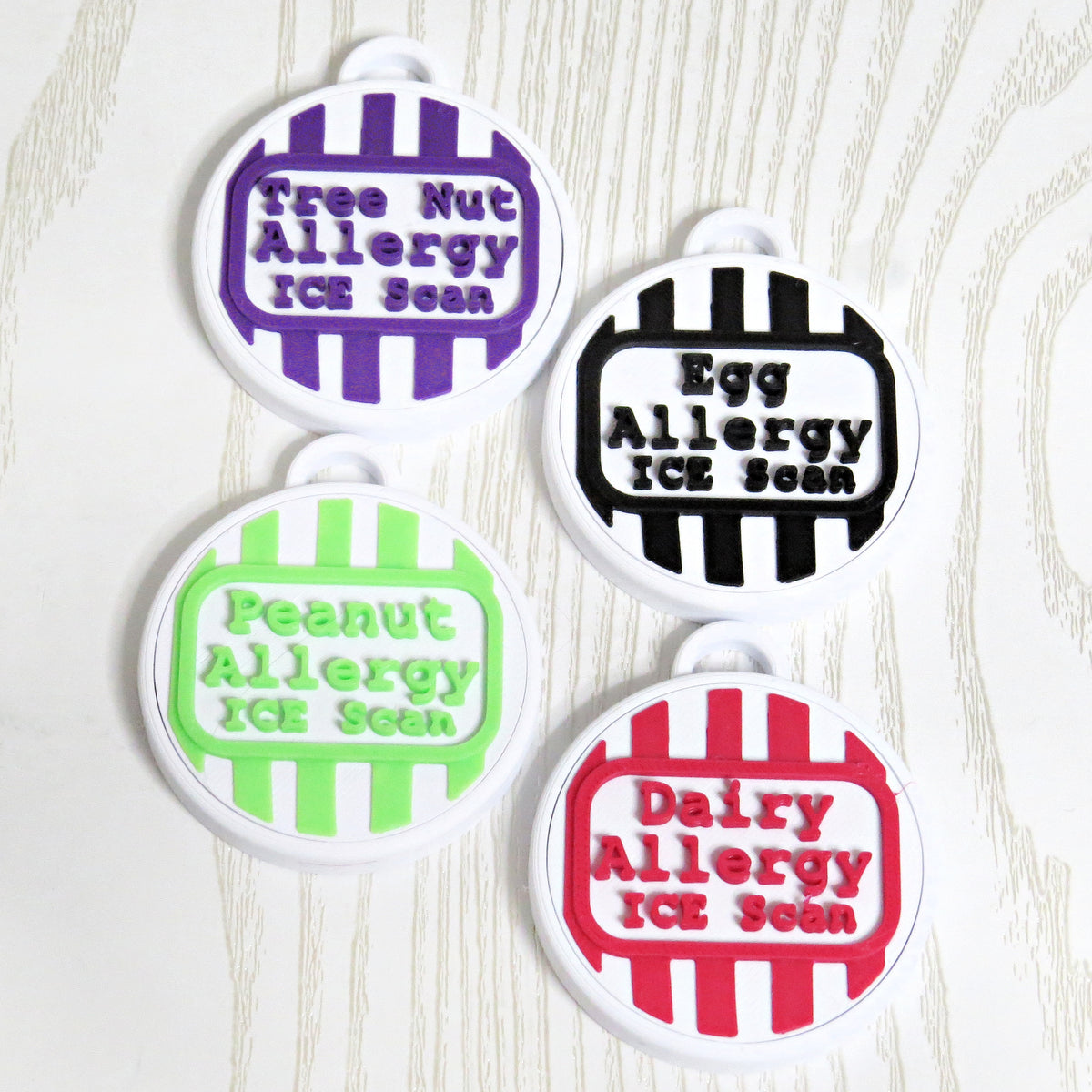 Four round striped allergy bag tags in purple, black, green, and red with raised allergy lettering and ICE Scan text