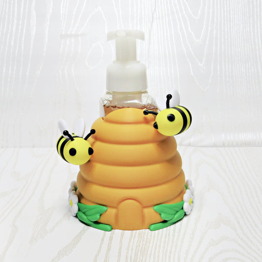 Beehive foaming soap holder with bees and flowers holding soap bottle on kitchen counter