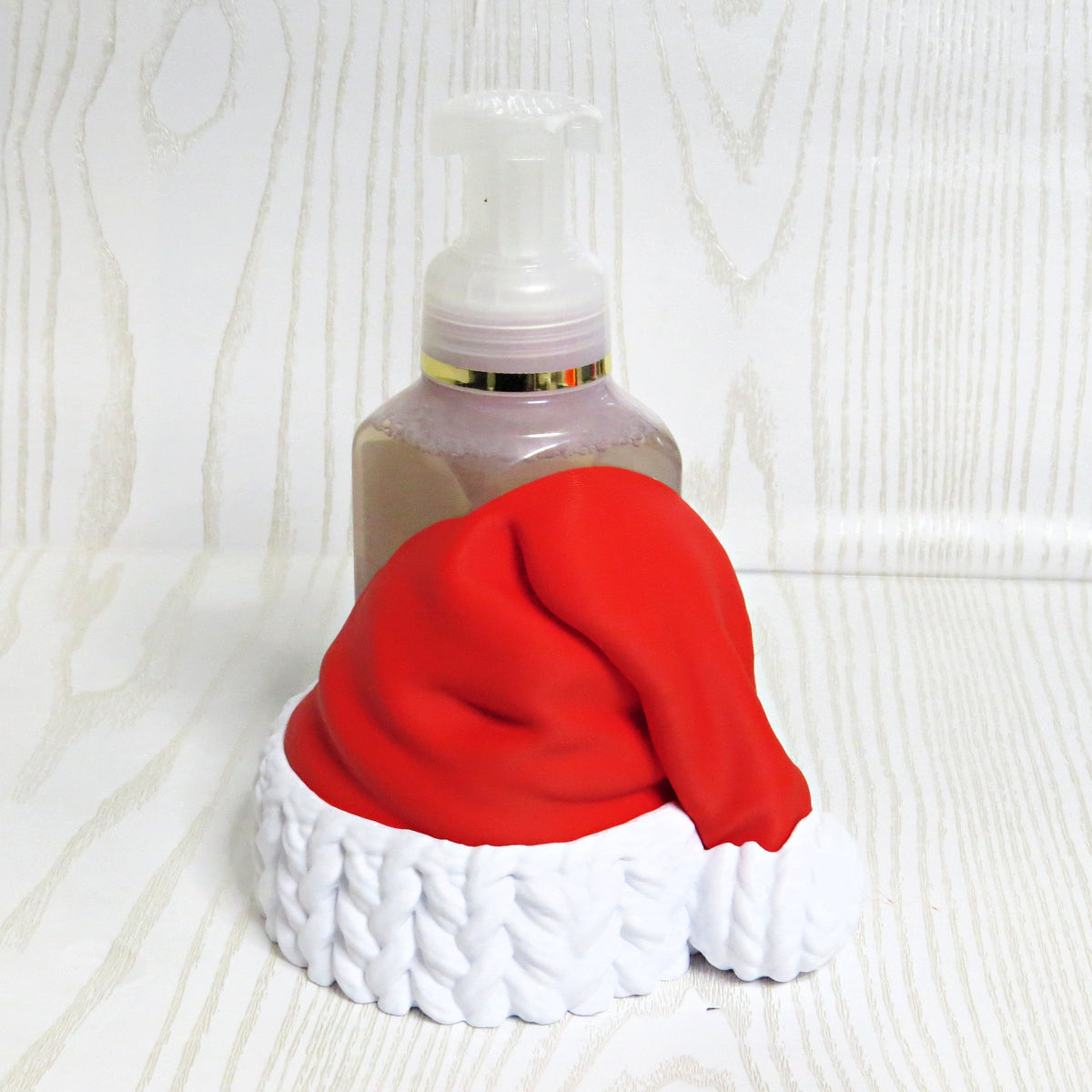 Red Santa hat with white knit cuff foaming soap bottle holder with a soap bottle behind it